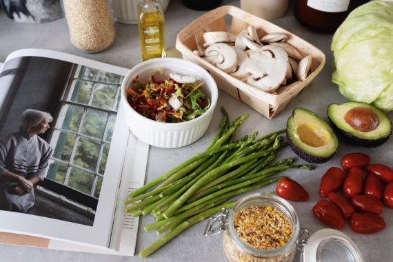 A selection of fresh vegetables and a cookbook in a kitchen setting, promoting healthy cooking.