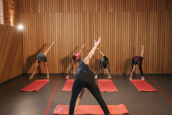 Yoga class with diverse adults stretching on mats in a cozy wooden studio.