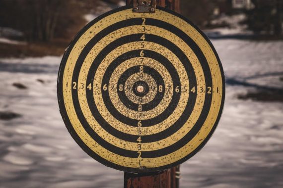 Yellow target for shooting with black circles and numbers on wooden post in countryside with snowy ground on winter day